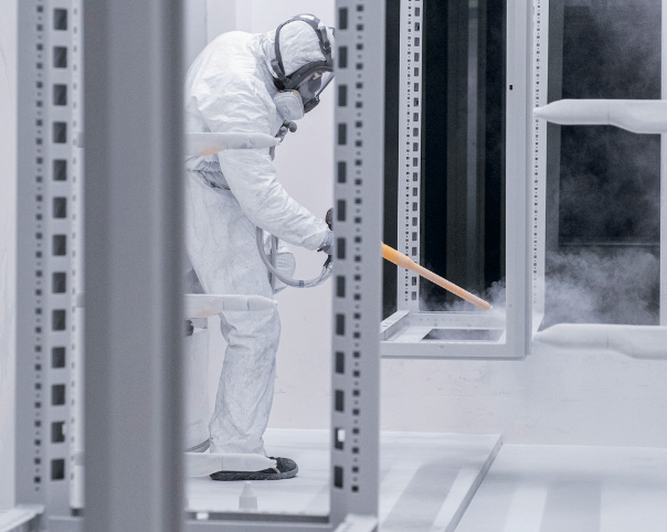 Technician applying protective coating to an enclosure frame in a controlled finishing booth